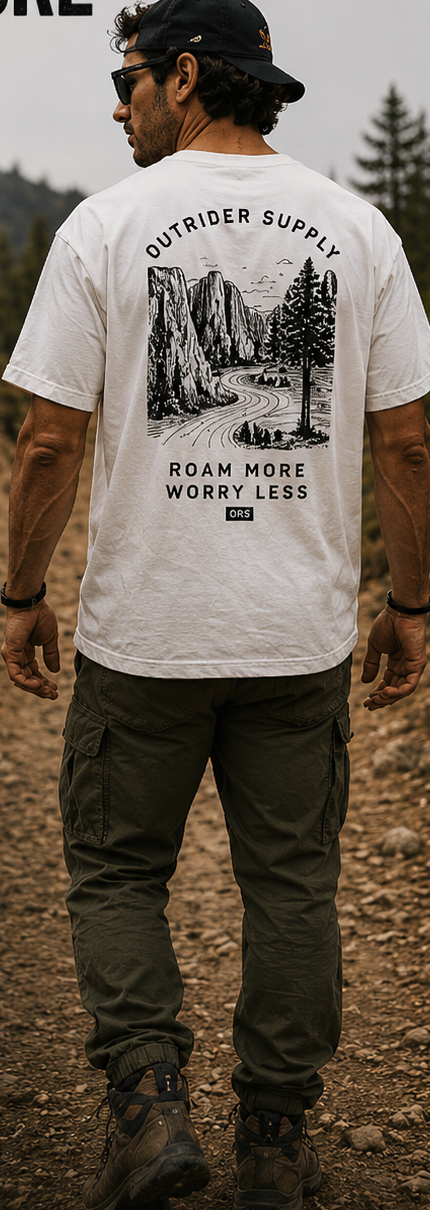 Male model wearing a forest-green graphic tee with a mountain back print beside an alpine lake